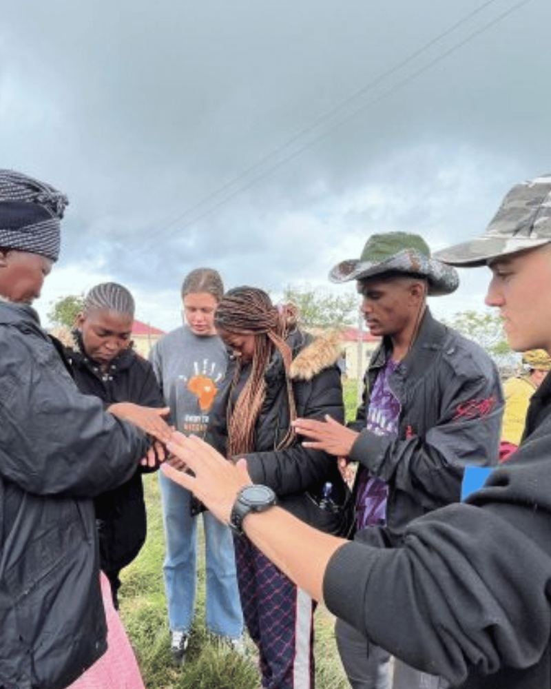 Faith Missions team and community members praying together, hands joined