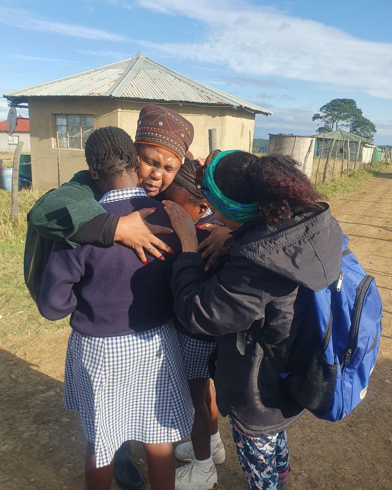 Two women embracing and praying over learners in school uniform