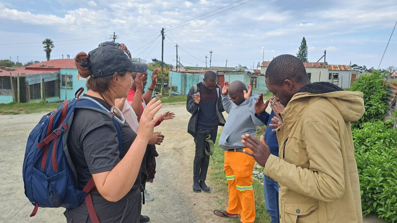 Mission team praying with a group of men on a township street