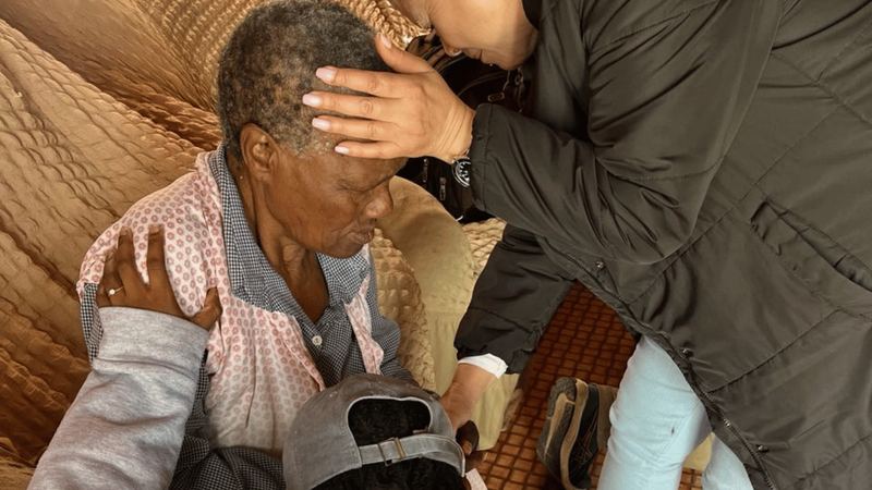 Team praying over an elderly man in his home